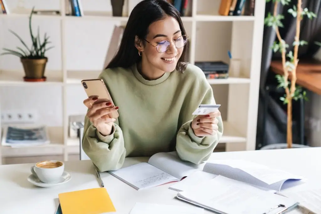 Woman holding her phone and smiling while looking at her credit card
