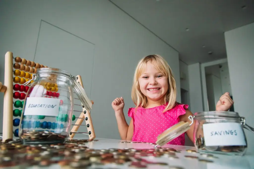 A child looking at two jars of change labeled "savings" and "education"