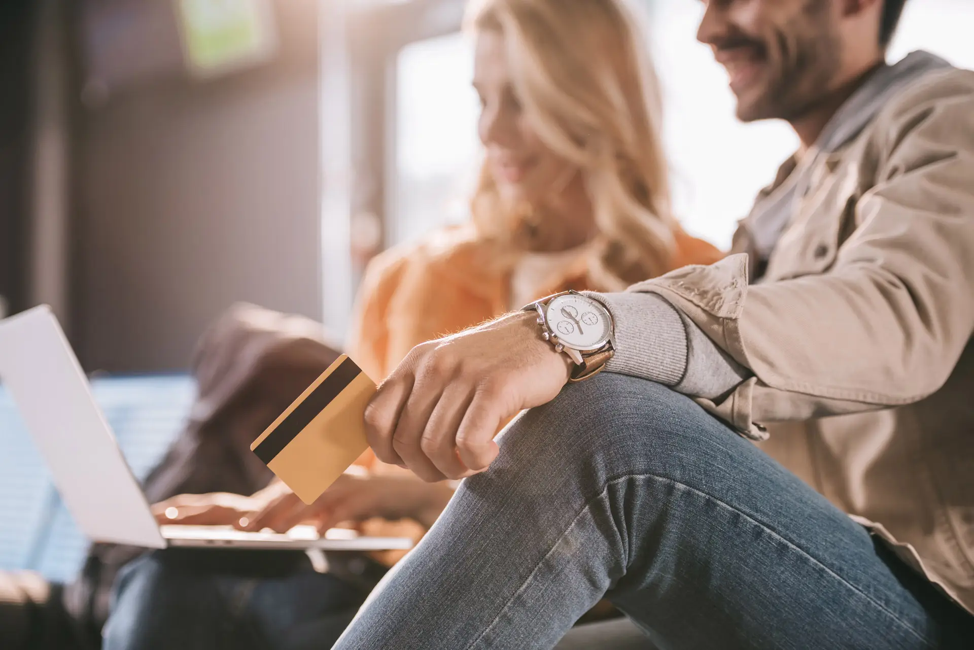 Man holding a credit card while a woman next to him uses a laptop