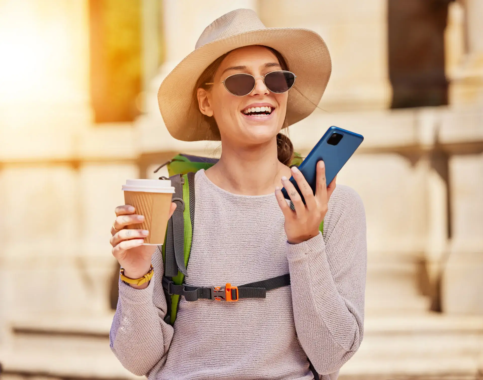 Backpacker smiling with a coffee in one hand and a phone in the other